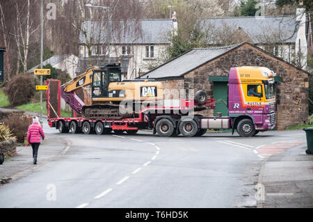 A low loader delivering a tracked excavator to a nearby quarry, negotiating a tight left hand turn. Stock Photo