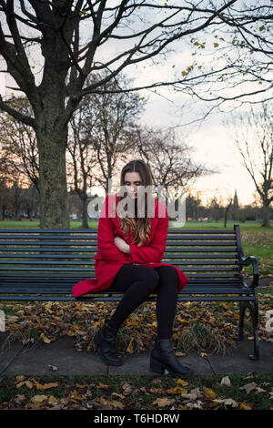 A young woman sitting on a bench in a park, with lots on her mind, feeling isolated and anxious. Stock Photo