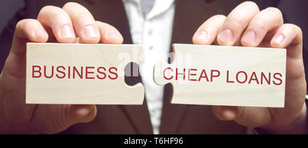 Businessman collects wooden puzzles with the words Business and cheap loans. Cheap and affordable loans to support small and medium businesses. Marsha Stock Photo