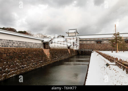 View along moat to the Hashizume-mon Tsuzuki Yagura, gate and turret at Kanazawa castle, daytime after snowfall. Dark grey clouds overhead. Stock Photo