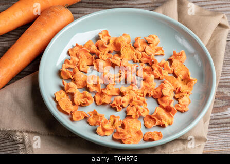 Close-up round turquoise plate with carrot chips on beige fabric and two whole carrots on old wooden table. Stock Photo