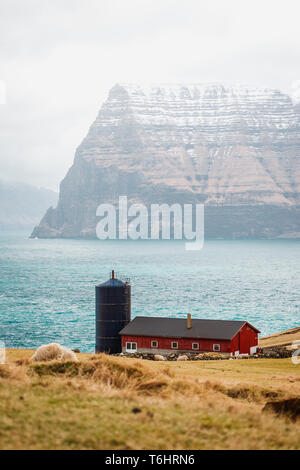 Small farm in the village of Trøllanes near Kallur lighthouse on Kalsoy island with view onto the high mountains of Kunoy islands  (Faroe Islands) Stock Photo