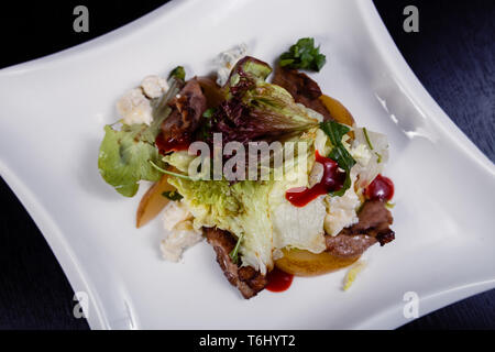 Appetizing salad sliced with pear slices of prosciutto pear arugula and parmesan on white plate Stock Photo