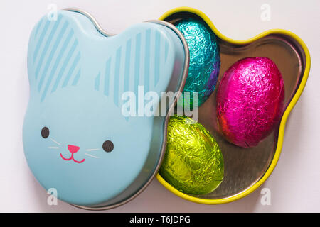 Easter Bunny tin with lid removed showing three foil covered mini Easter eggs isolated on white background - 3 foiled solid milk chocolate mini eggs Stock Photo