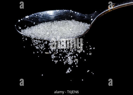 closeup of sugar falling from a teaspoon on a black background Stock Photo