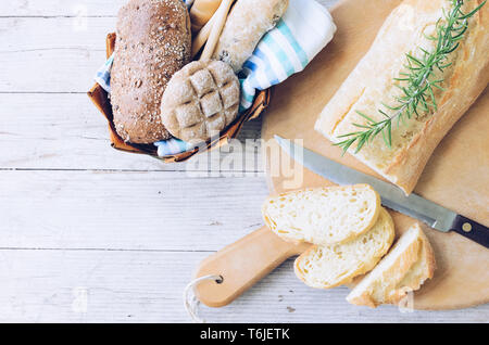 Fresh sliced bread and cutting knife on wooden board on the rural kitchen table. Assortment of freshly baked crusty loaves of bread and buns. Traditio Stock Photo
