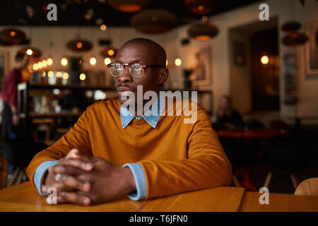 Warm toned portrait of pensive African-American man sitting at table in bar, copy space Stock Photo