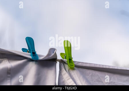 White clothes hung out to dry on a washing line and fastened by the clothes pegs against the blue sky in the bright warm sunny day Stock Photo