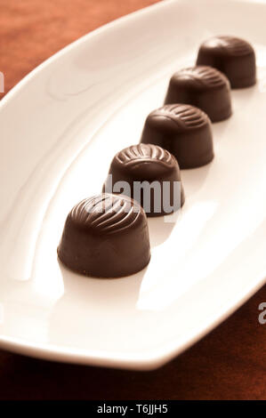 row of chocolate bonbons on a white porcelain plate Stock Photo