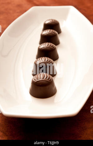 row of chocolate bonbons on a white porcelain plate Stock Photo