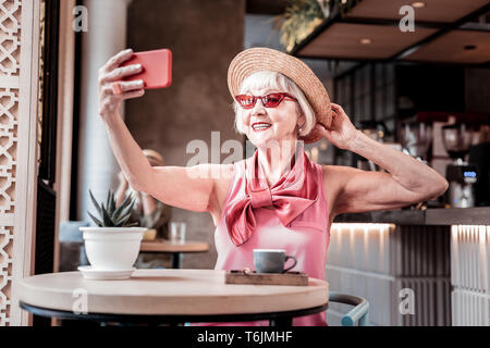 Beaming old woman wearing pink blouse and making selfie Stock Photo