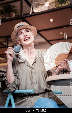 Cheerful fashionable senior lady carrying white fan Stock Photo
