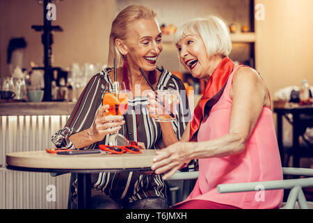 Blonde joyful lady in striped blouse talking to her short-haired friend Stock Photo