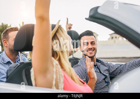 Happy friends having fun in convertible car at sunset in vacation - Young rich people making party and dancing in auto cabriolet during road trip Stock Photo