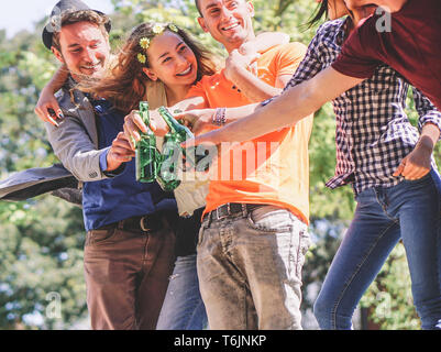 Group of friends cheering and drinking beers outdoor - Happy young people having fun toasting bottles of beer and laughing together Stock Photo