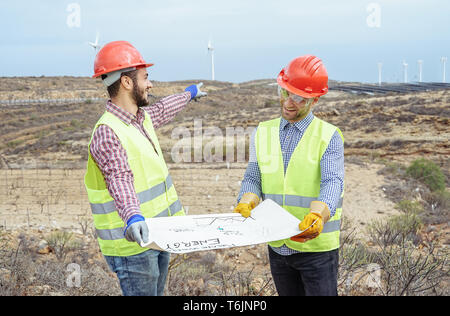 Workers engineers reading and talking about the new renewable energy project - Builders discussing and showing how to build windmill and panels solar Stock Photo