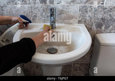 hands holding cleaning spray and sponge, cleaning a dirty bathroom sink Stock Photo