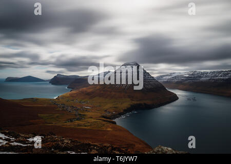 Long exposure panoramic view from Kap Enniberg towards the village Viðareiði, its fjord with snow-covered mountains (Faroe Islands, Denmark, Europe) Stock Photo