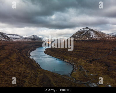 Aerial panoramic view of the fjord of Funningsfjørður with dramatic cloudy sky and snow-covered mountains (Faroe Islands, Denmark, Europe) Stock Photo