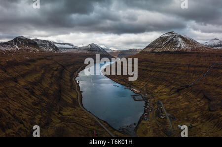 Aerial panoramic view of the fjord of Funningsfjørður with dramatic cloudy sky and snow-covered mountains (Faroe Islands, Denmark, Europe) Stock Photo