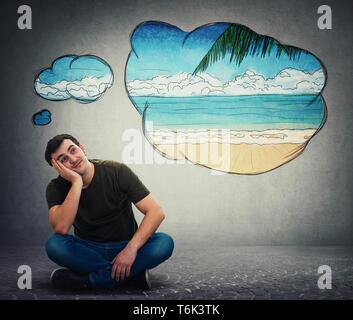Young man dreamer sitting on the floor holding hand under cheek leaning on a side looking up dreaming of new travel destination as thought bubble clou Stock Photo