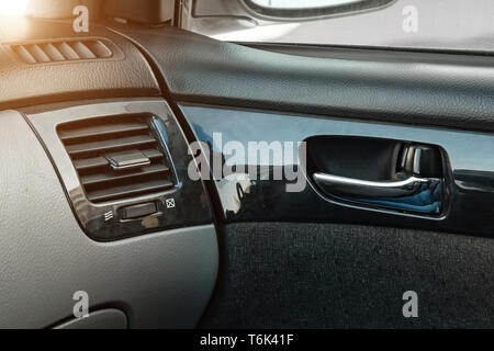 A close-up view of a part of the interior of a modern luxury car with a view of a silver-colored door handle on a chrome finish with black wood trim a Stock Photo