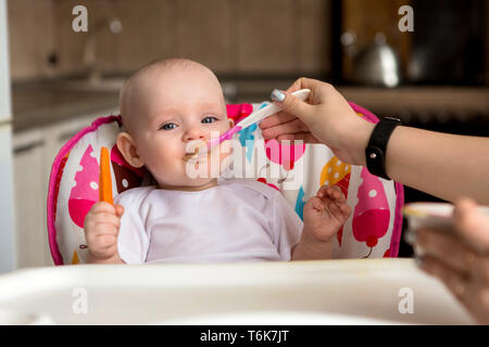 baby is 8 months and eats independently.the first lure baby.The baby with blue eyes does not want to eat vegetable puree.mom feeds from a small child' Stock Photo