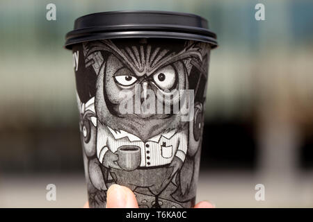 Black paper disposable coffee cup with a drawn owl in hand on a blurred background outdoor Stock Photo