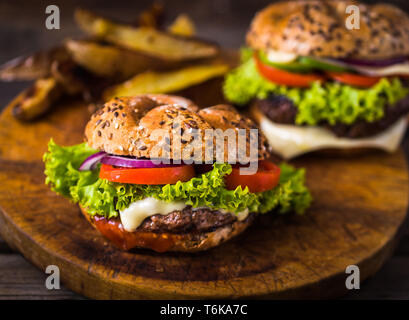 Home made hamburger with green salad and with american potatoes behind. Brown wooden background. Stock Photo