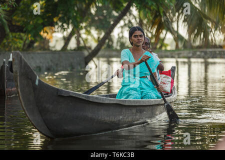 Closeup of woman in turquoise sari paddling canoe with older woman paddling on the other side in jungle river waterway in India Stock Photo