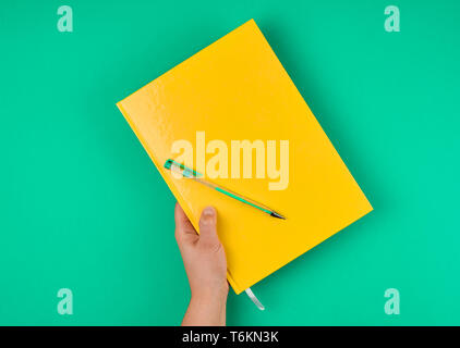 hand holds large closed yellow notebook and green pen, top view Stock Photo