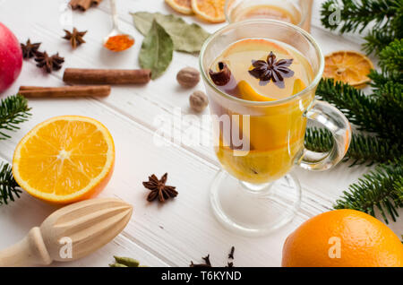 Christmas hot white mulled wine in glass with orange, honey, cinnamon sticks and star anise with spices and ingredients on white wooden background. Sp Stock Photo