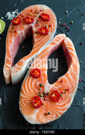 Two fresh raw salmon steaks with pepper corns, salt, lemon and olive oil on black background. Healthy food, diet concept. Preparation for cooking fish Stock Photo