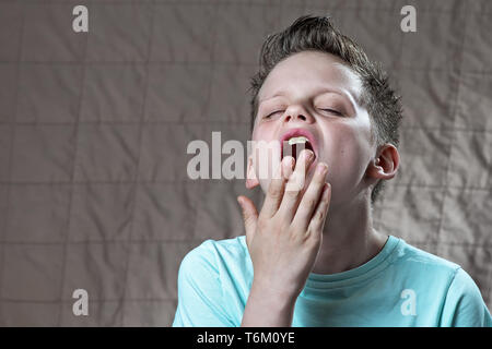 the boy in the blue t-shirt is tired, wants to sleep and yawns Stock Photo