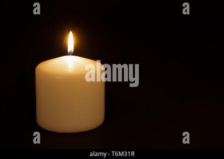 White candle burning against a black background Stock Photo