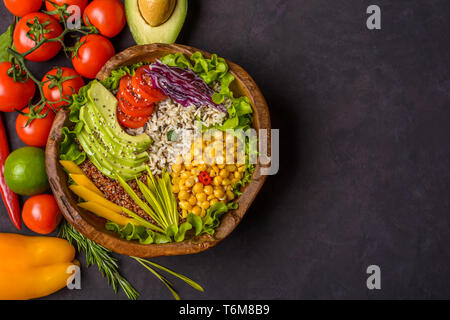 Wooden bowl with chickpea, avocado, wild rice, quinoa, tomatoes, greens, cabbage, lettuce on dark stone background. Vegetarian superfood. Top view cop Stock Photo