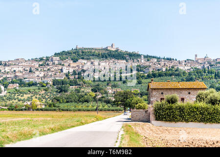 Road leading to village city of Assisi in Umbria, Italy cityscape of church during sunny summer day farm rural landscape Etruscan countryside Stock Photo