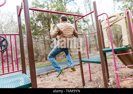 Young fit man exercising doing chin pull ups on bar in playground park in autumn winter or spring calisthenics Stock Photo