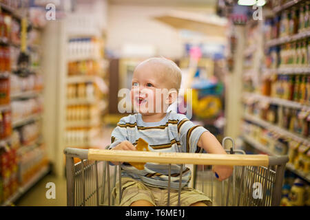 Male toddler sitting in a shopping cart looking delighted Stock Photo