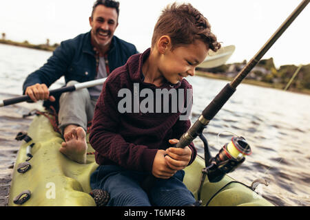 Close up of a kid sitting in a kayak catching fish holding a fishing rod. Happy man rowing a small boat in a lake while his kid tries to catch fish us Stock Photo