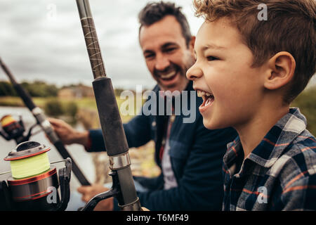 Close up of a smiling man fishing along with his son in a lake. Smiling man looking at his son enjoying fishing on a pleasant day. Stock Photo