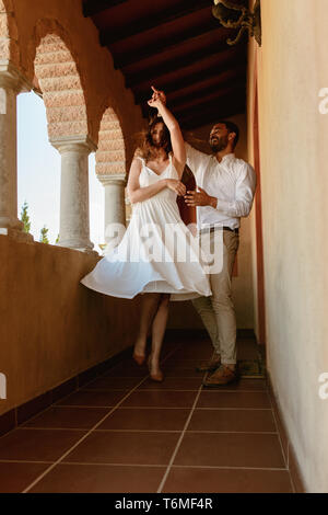 Happy couple dancing in the balcony of a building. Smiling man and woman on a date dancing together. Stock Photo
