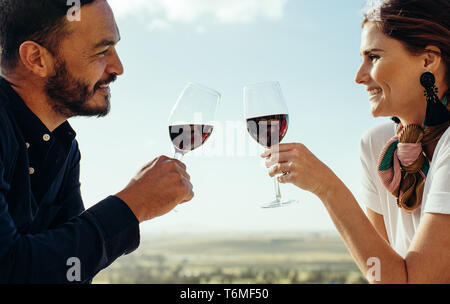 Cropped shot of a happy couple sitting together with glass of wine. Side view of a couple talking to each other toasting glass of red wine. Stock Photo