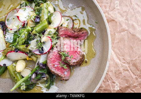 Traditional spring salad with barbecue dry aged sliced fillet steak and green and white asparagus as top view on a plate with co Stock Photo