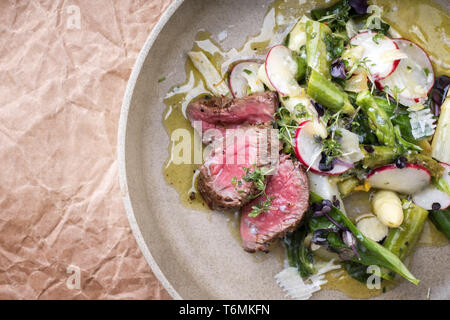 Traditional spring salad with barbecue dry aged sliced fillet steak and green and white asparagus as top view on a plate with co Stock Photo