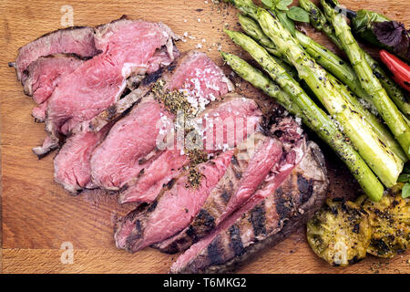 Traditional barbecue dry aged sliced roast beef steak with green asparagus and tomatoes as close up on a wooden board Stock Photo