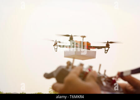 Closeup of blurred hands opertaing drone transmitter, receiver controller, controller in out of focus while drone is in focus at background. Stock Photo