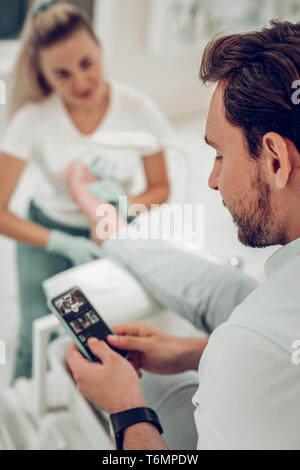 Dark-haired curious man checking his smartphone while long-haired master Stock Photo