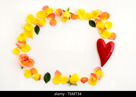 Frame made of roses, rose petals and wooden red heart, on white background. Stock Photo