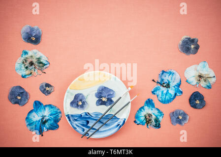 Blue pansies and painted ceramic plate, on peach canvas background with copy space. Stock Photo